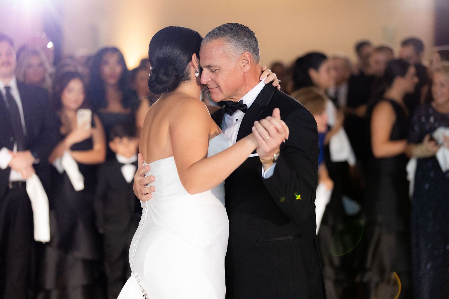 Elegant couple shares their first dance at a wedding reception with guests watching in the background.