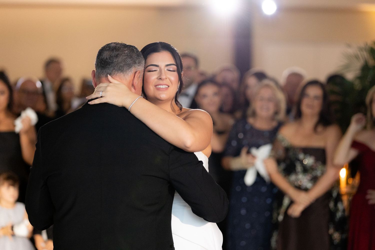 Wedding guests dance and celebrate on a crowded reception dance floor under ambient lighting.