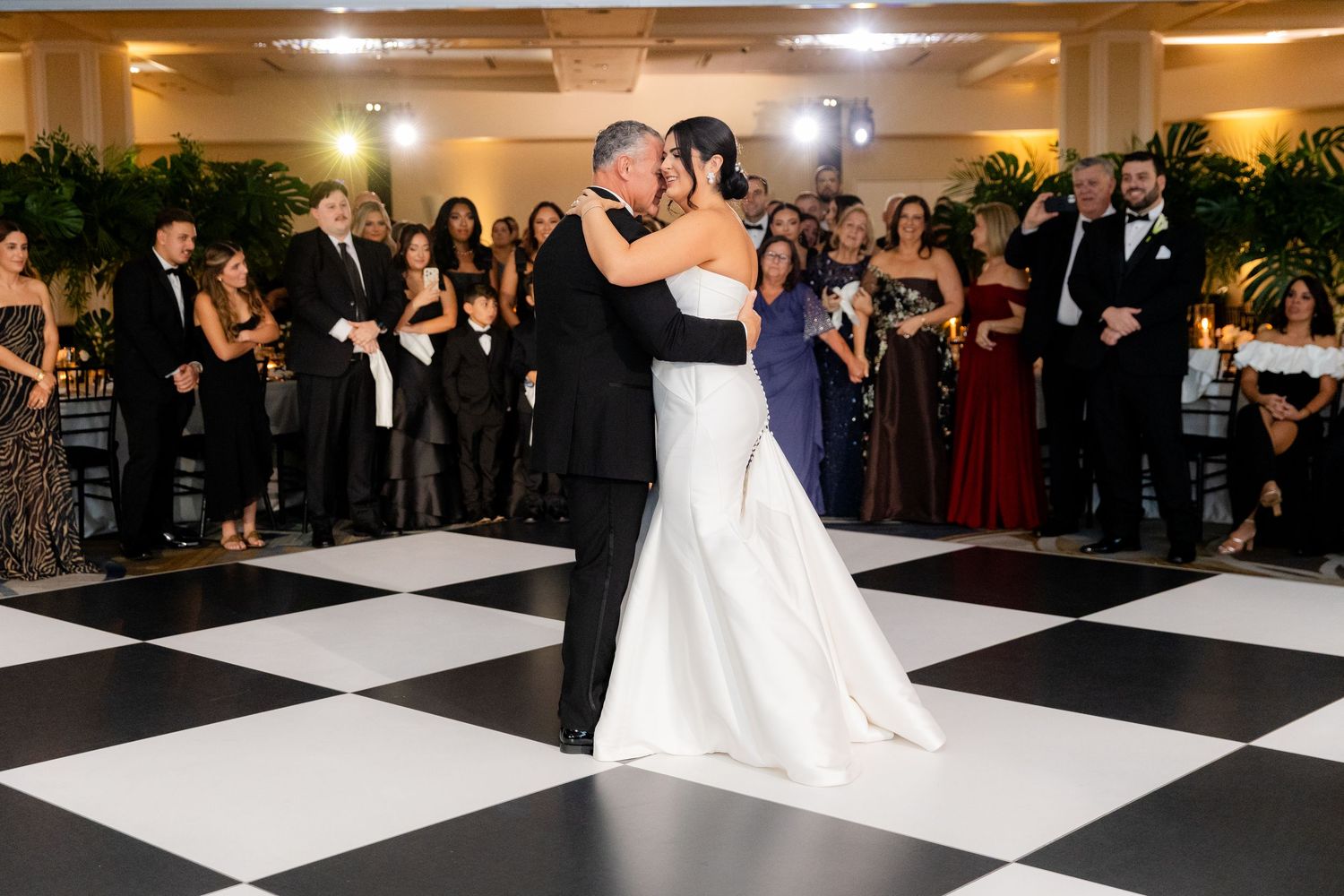 Wedding reception guests dance on a black and white checkered dance floor in an elegant ballroom.