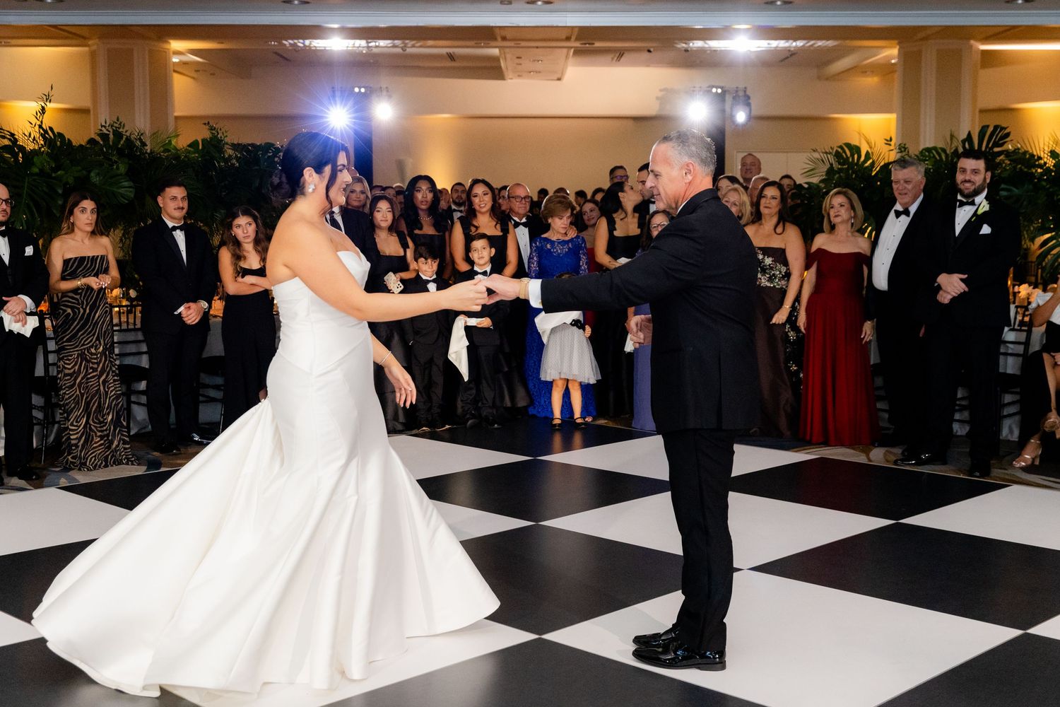 Wedding reception dance floor with black and white checkered tiles and formal guests gathered around the edges.