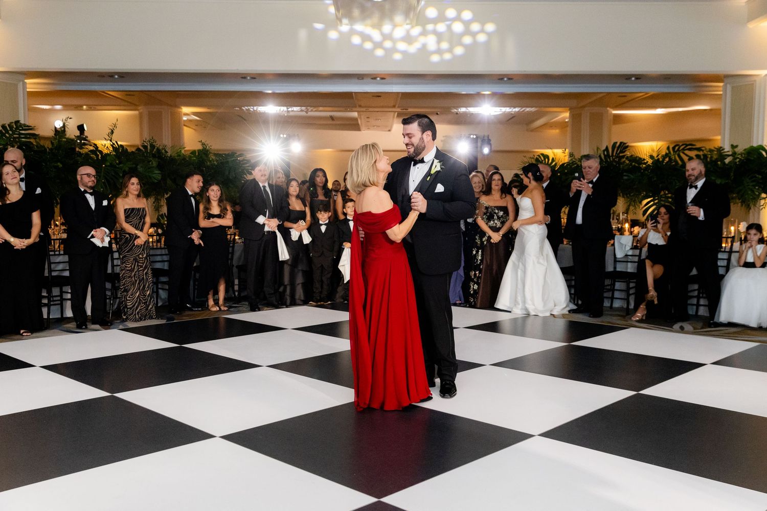 Wedding guests dance and celebrate on an elegant black and white checkered dance floor at a reception.