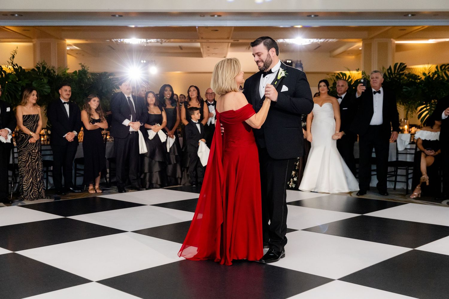 Wedding reception with dancers on a black and white checkered floor lit by warm ballroom lighting.