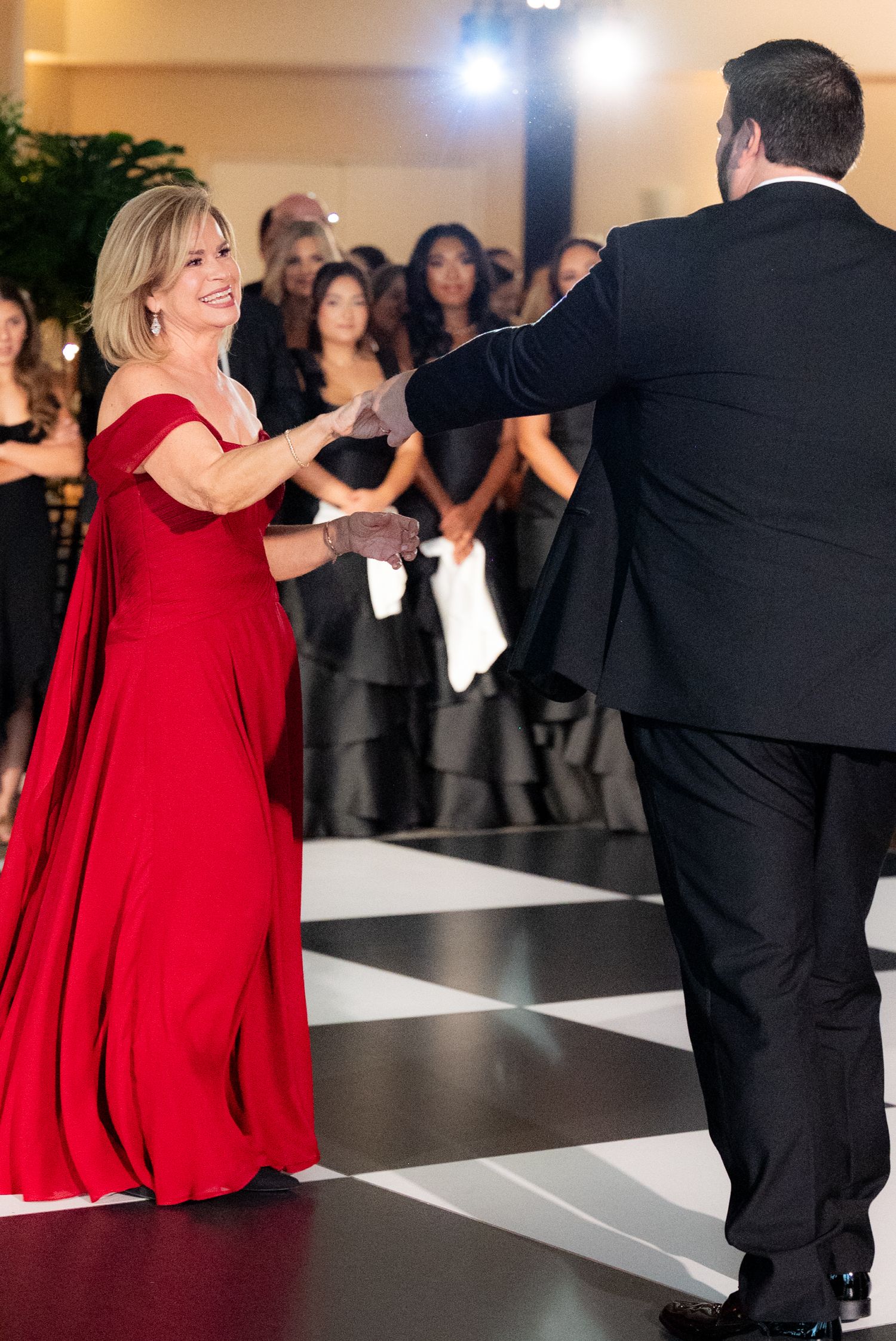 Couple dancing at reception with person in red dress creating dramatic movement on dance floor.