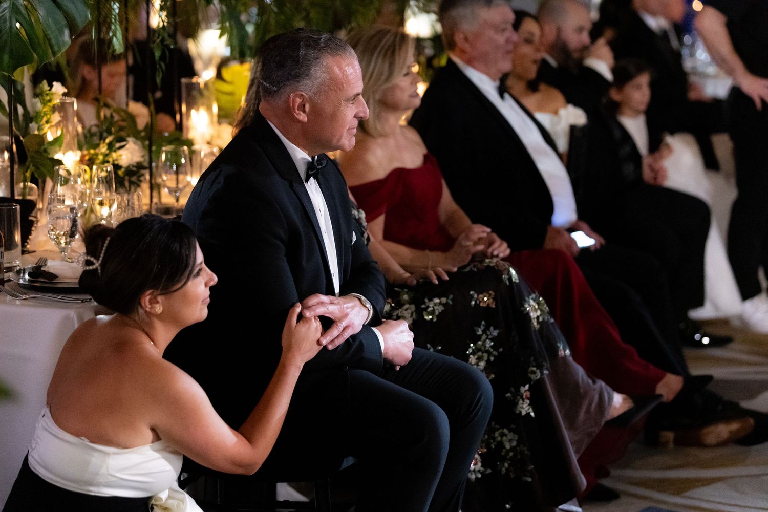 Wedding guests gather at elegant reception tables decorated with floral centerpieces and candlelight.