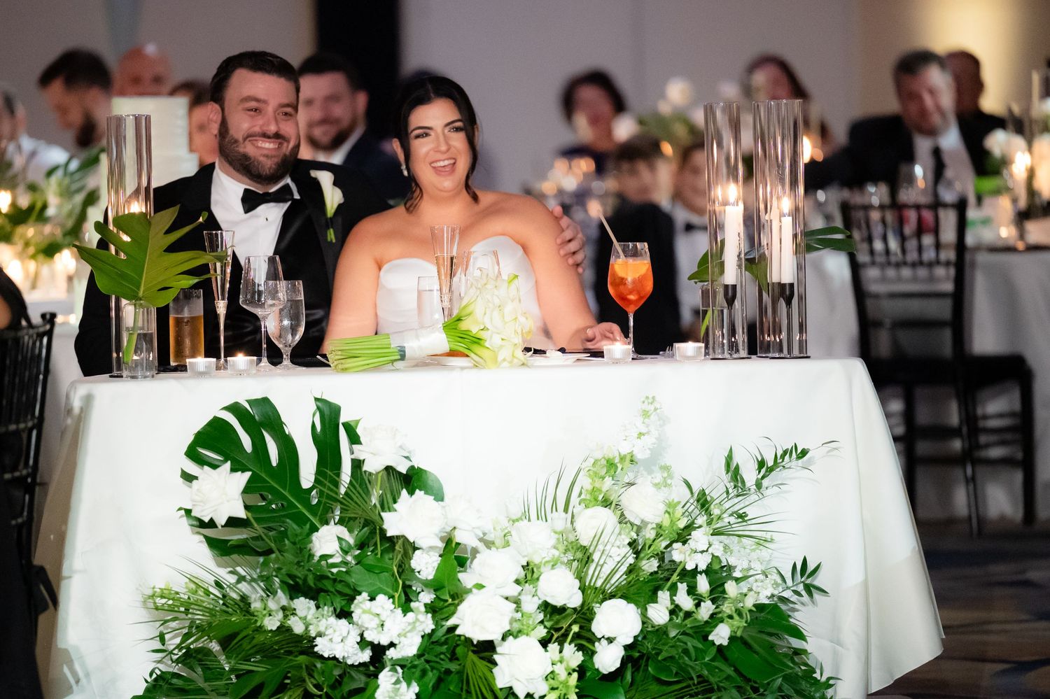 Wedding reception table settings with white linens, tropical monstera leaves, and orchid floral centerpieces.