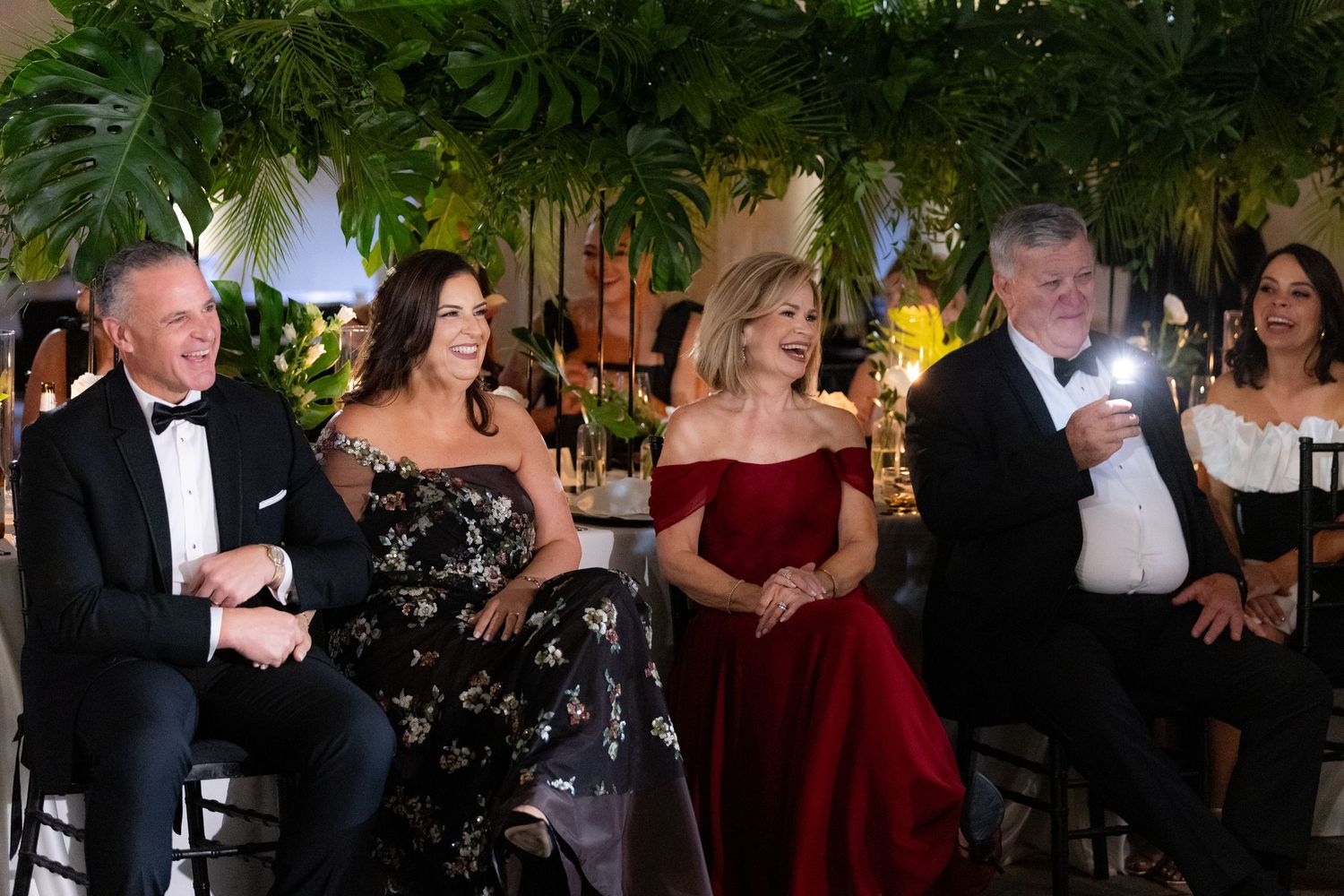 Formal evening event with guests in black tie attire seated at an elegant table with tropical decorations.