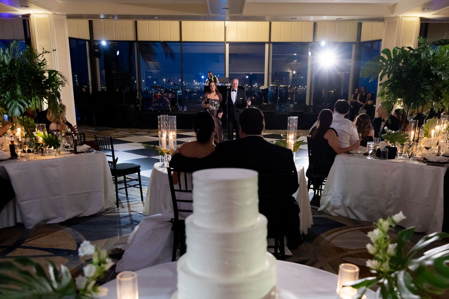 An elegant wedding reception venue setup with white decor, floral arrangements, and ambient lighting at dusk.