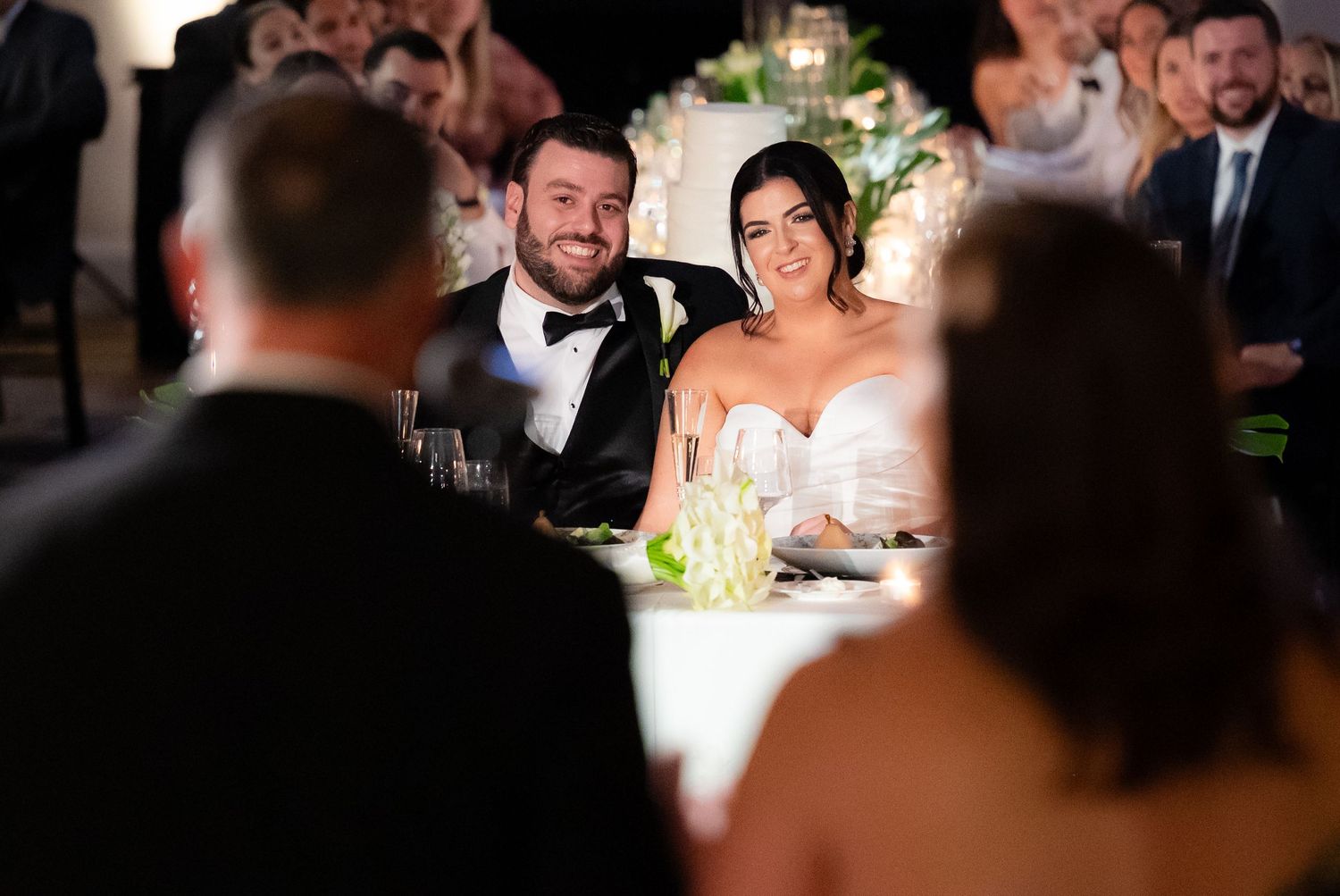 Formal reception tables filled with guests enjoying conversation and dinner at an evening wedding celebration.