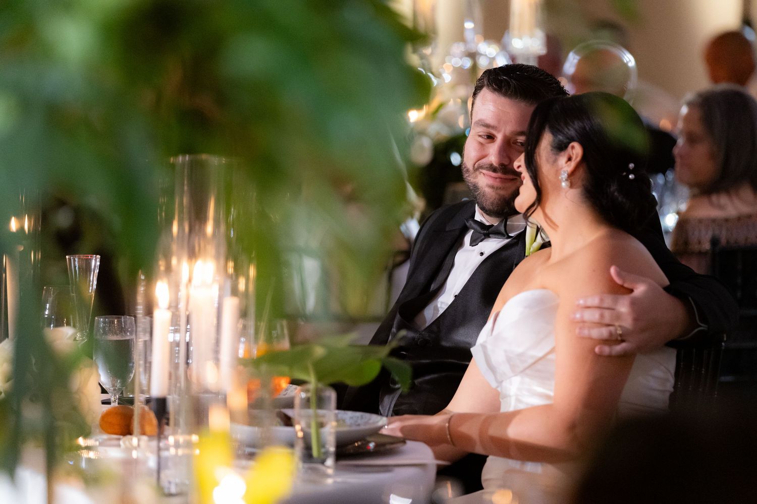 Intimate wedding reception moment captured through greenery with soft candlelight on the dinner table.