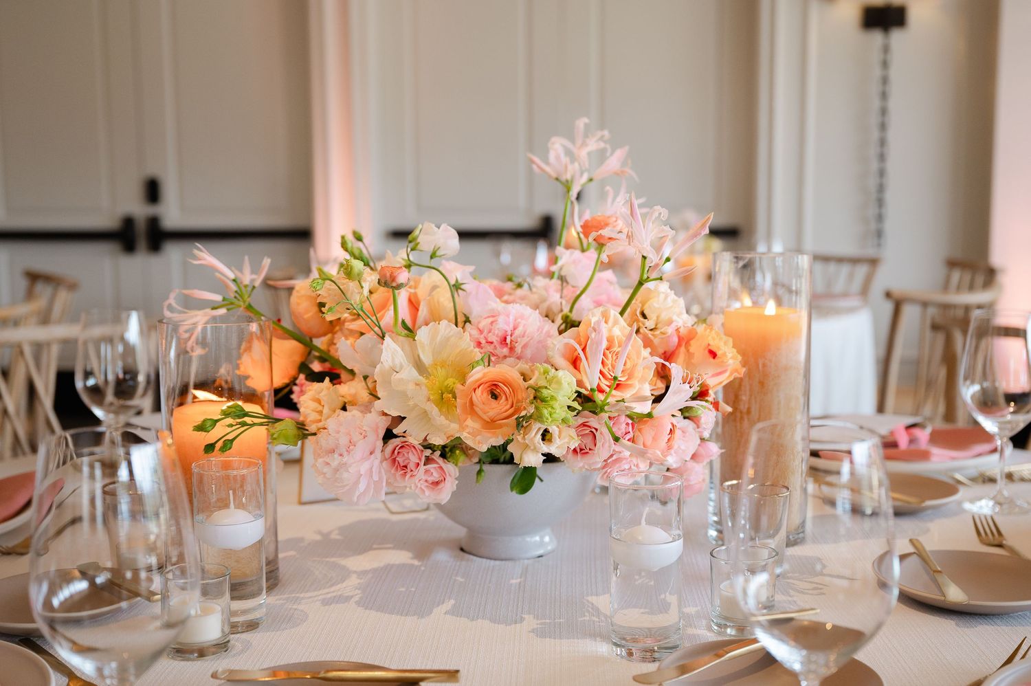 Elegant table setting with pink and peach floral centerpieces and glassware for a special occasion.