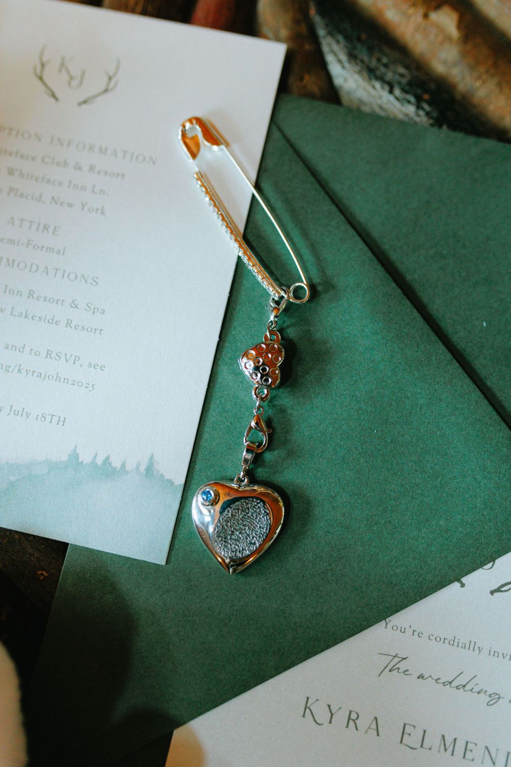 Wedding invitation details with decorative jewelry on dark green fabric background.