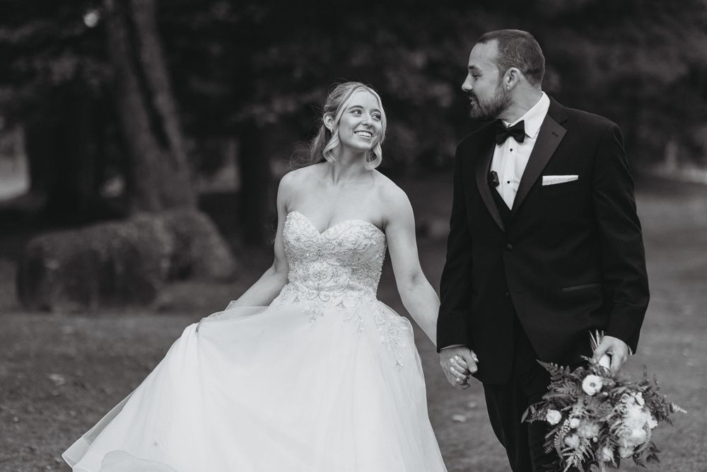 Black and white wedding photo of couple embracing on a dock with water views.