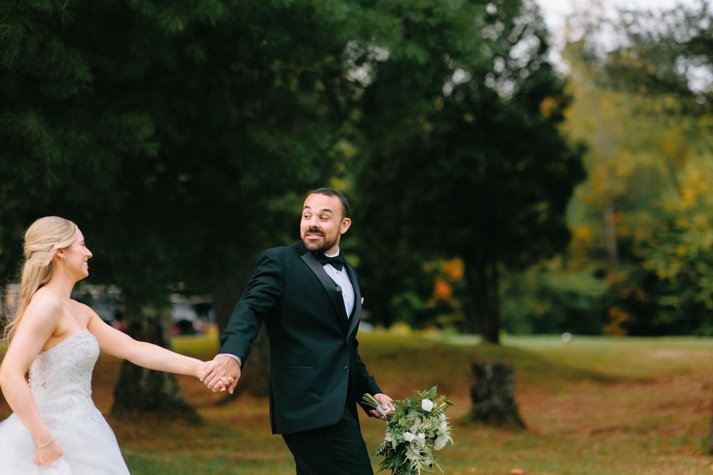Wedding couple embracing outdoors during autumn with fall foliage in background.