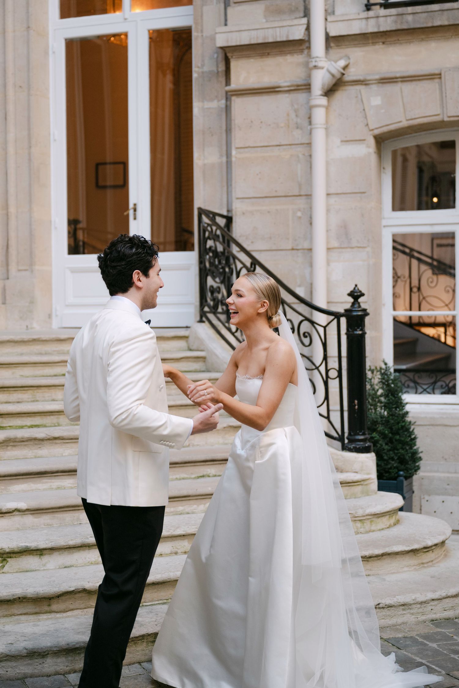 A couple in wedding attire shares a romantic dance moment on an elegant stone porch with ornate railings.