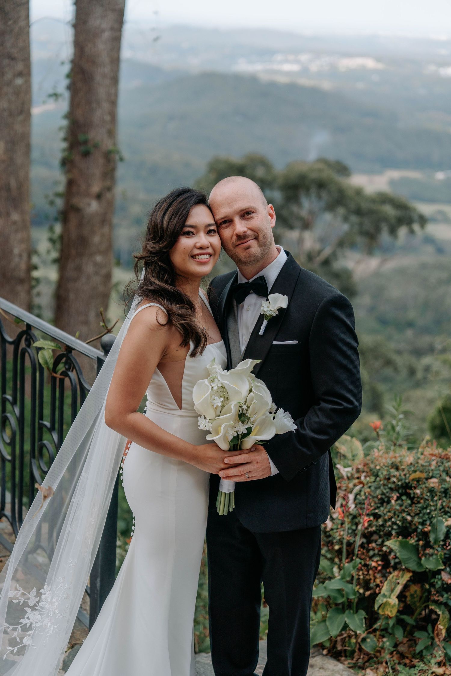 A romantic wedding moment captured against a scenic mountain backdrop with trees and blooming roses.