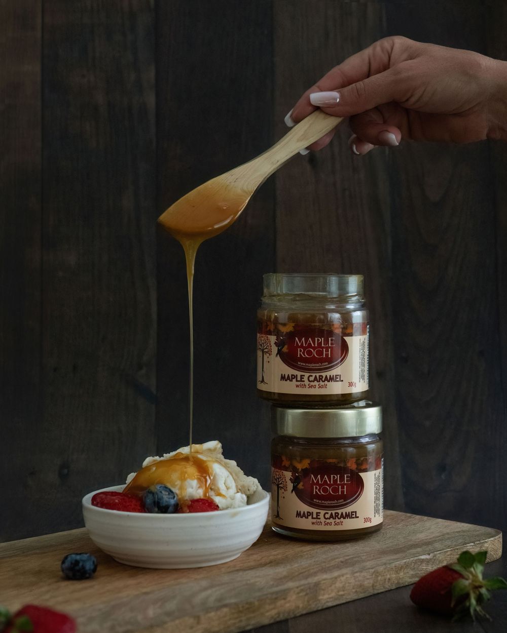 Hand drizzling Maple Roch maple caramel over vanilla ice cream  with berries beside two jars - Okanagan product photography by Tania Veitch.