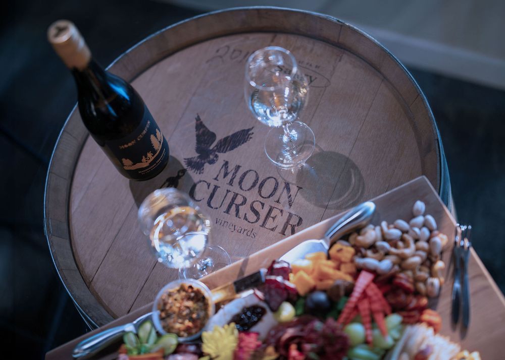 Moon Curser wine bottle and two glasses on glass-top barrel table with logo and charcuterie - Okanagan brand  photo.