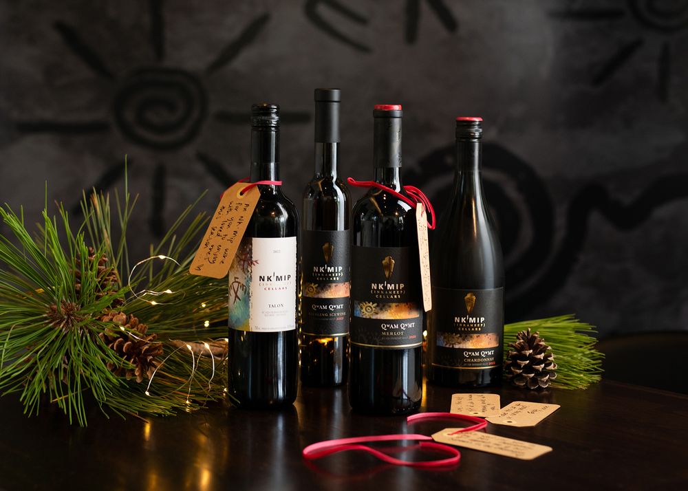 Four bottles of Nk’Mip Cellars wine styled with pine branches and gift tags for a holiday winery photography session in the Okanagan.