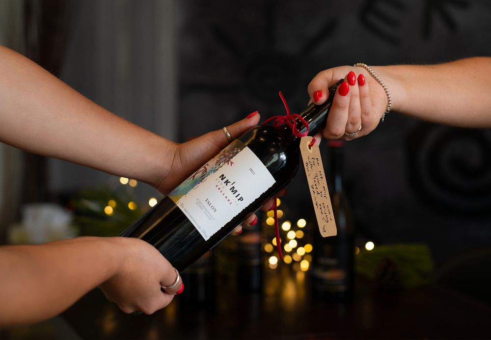Hands exchanging a bottle of Nk’Mip Cellars wine styled as a holiday gift.