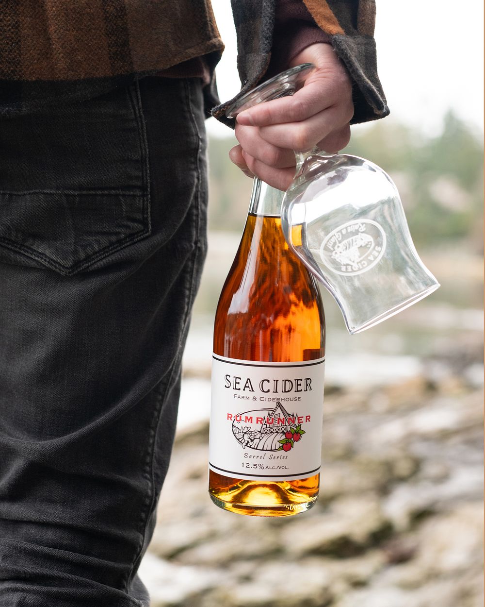 Man holding Sea Cider Rumrunner bottle and glass with ocean backdrop - Okanagan brand and product photography by Tania Veitch.