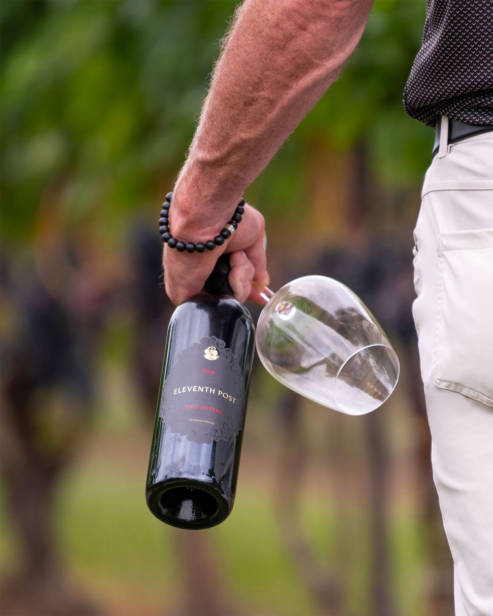 Man holding Two Sisters Vineyards Eleventh Post red wine bottle and glass in vineyard - Okanagan lifestyle photography by Tania Veitch.