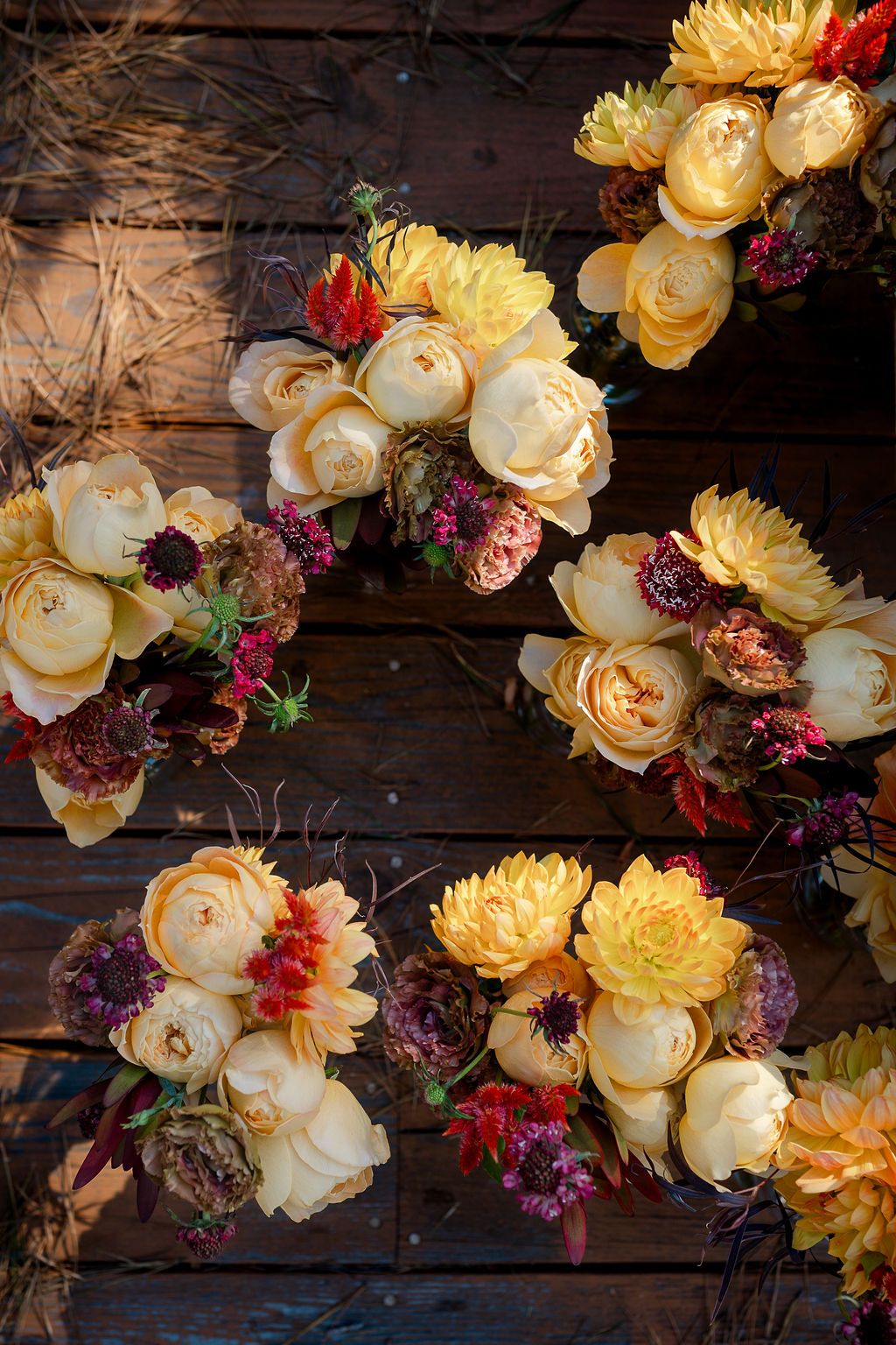 Blooming roses, peonies and lilacs in warm yellow, cream and burgundy hues arranged on a rustic wooden backdrop.