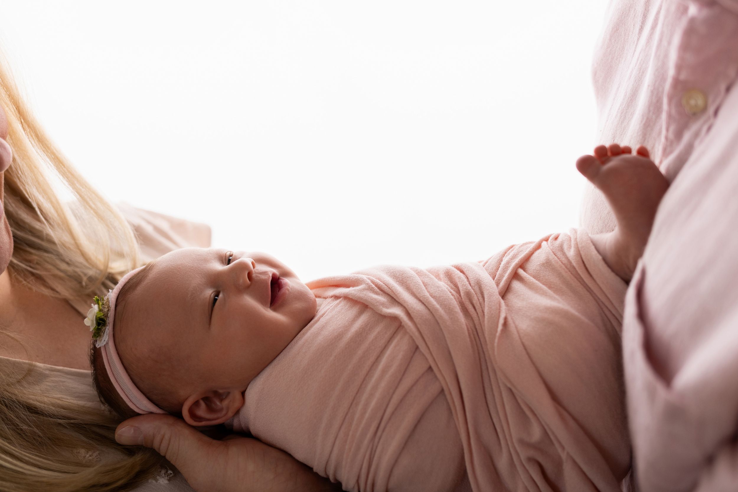 A joyful interaction between parent and newborn baby lying on soft bedding.