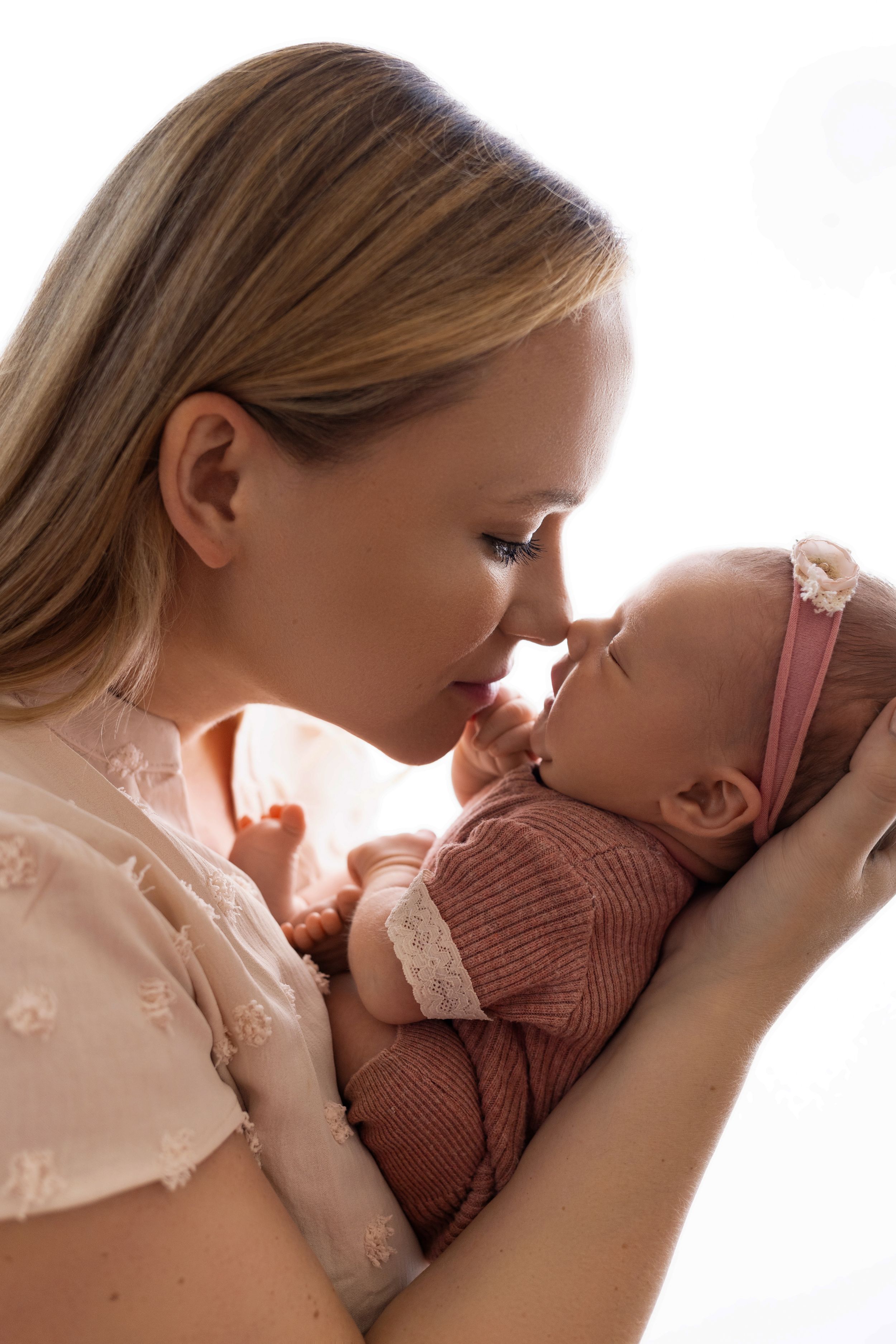 Mother and baby share an intimate moment in soft natural light while dressed in white and pink.