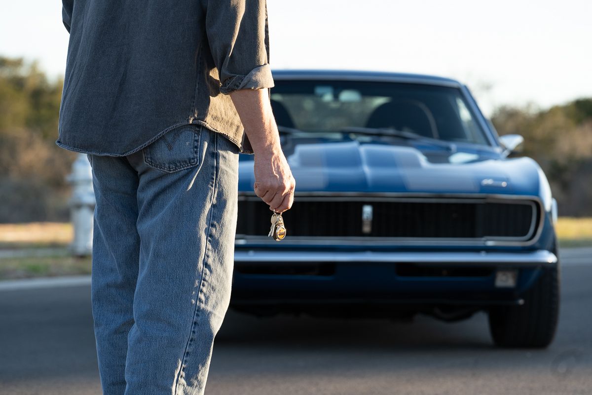 Classic black muscle car parked on an empty road at sunset.
