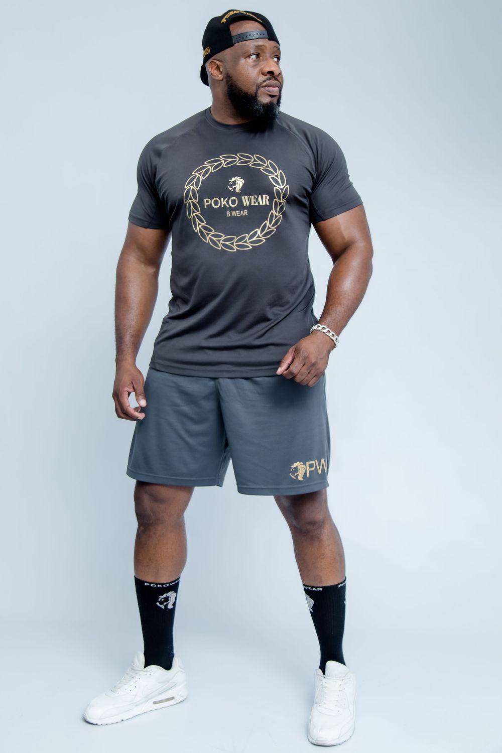 Athletic model wearing a dark gray workout set with a circular logo t-shirt and matching shorts against white backdrop.