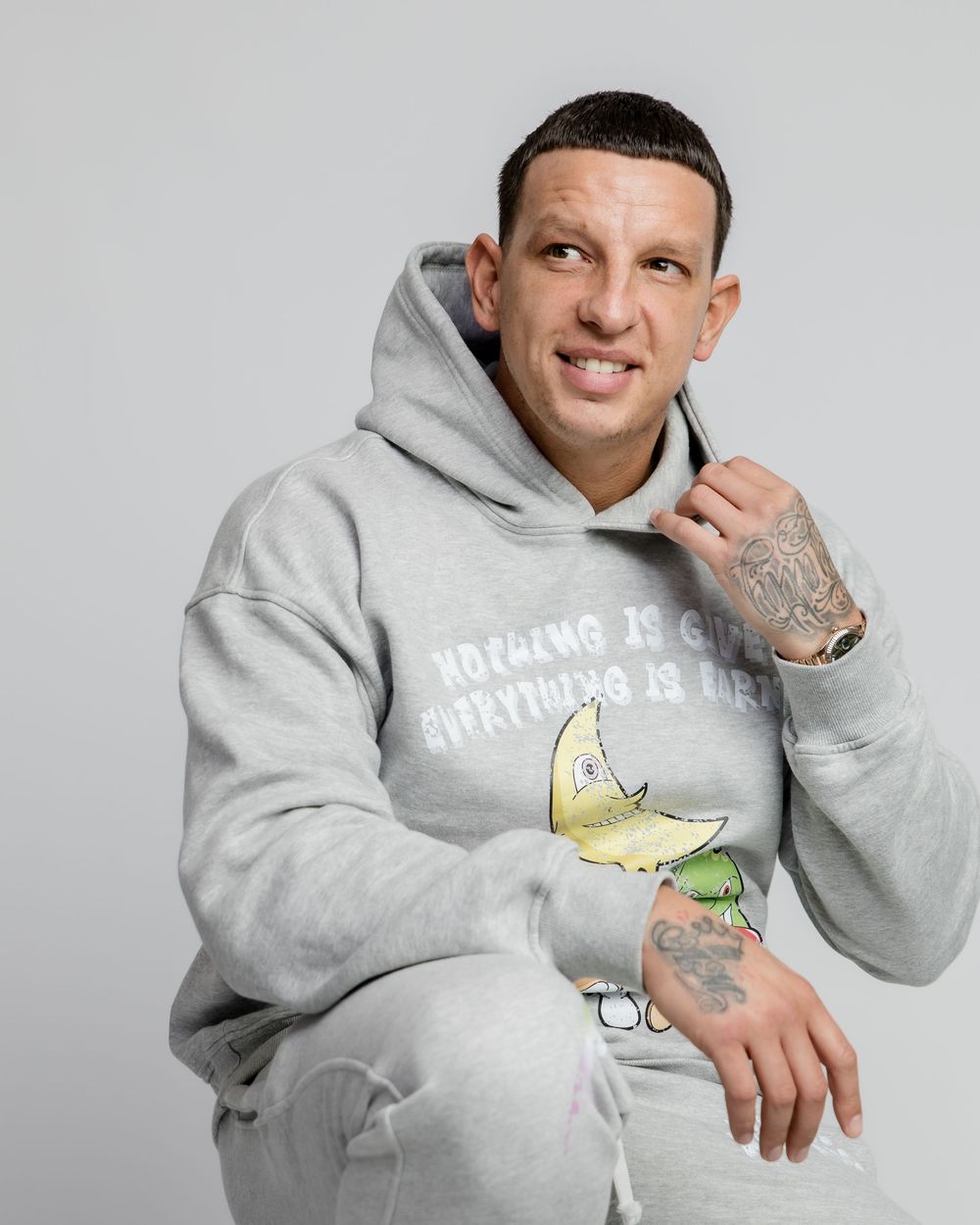 Athletic model wearing a light gray hoodie with cartoon graphic design poses against white background.