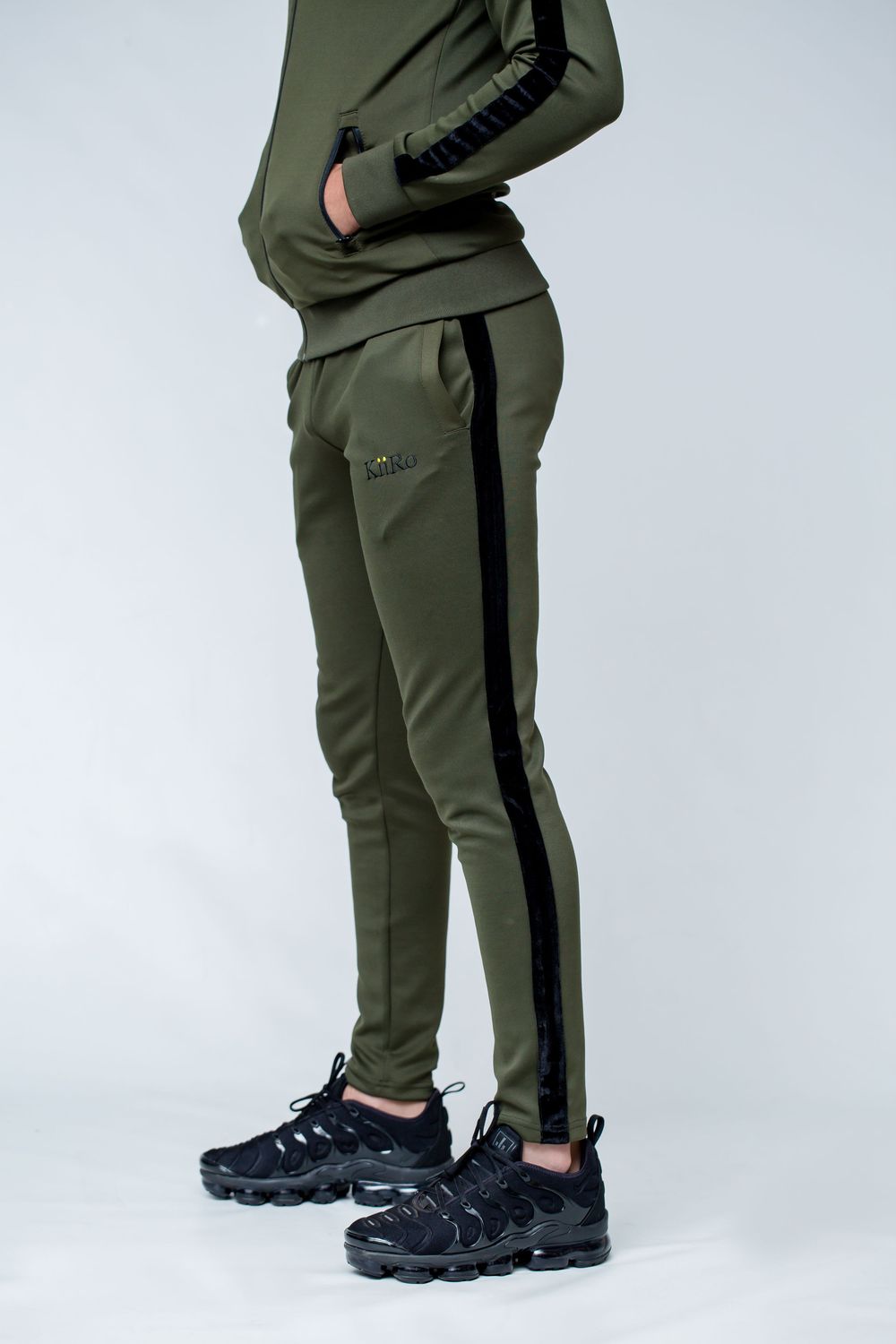 Athletic pants in olive green with black side stripes shown from different angles with black sneakers against white background.