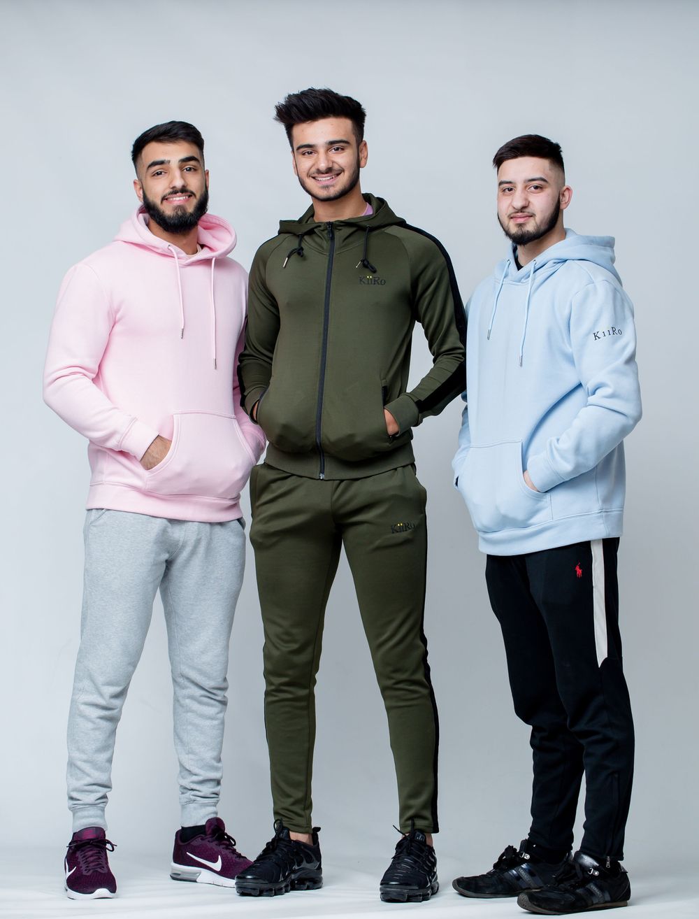 Three people pose in comfortable athleisure wear featuring hoodies and sweatpants in pink, olive green, and light blue colors.