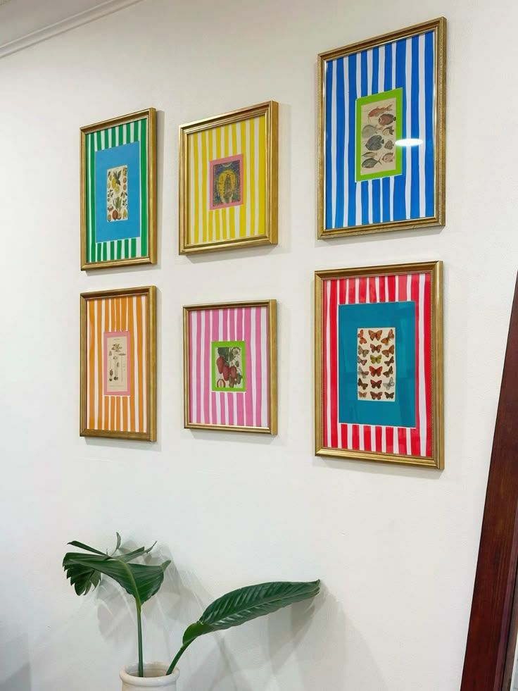 Colorful striped framed artwork gallery wall display with six frames in various colors and a tropical plant beneath.