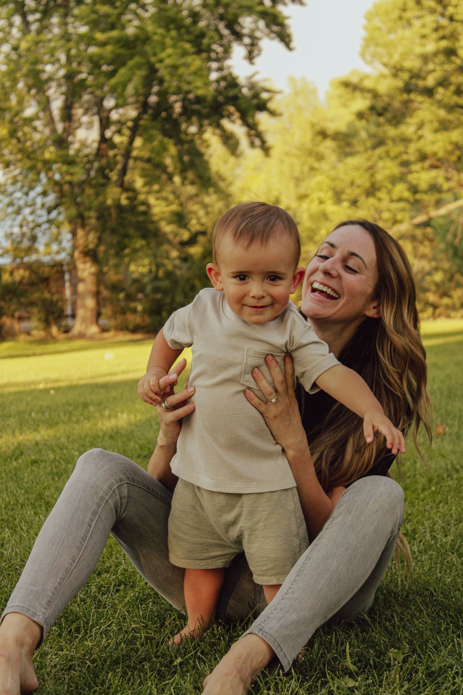A joyful moment shared between parent and child playing together on green grass in a sunlit park.
