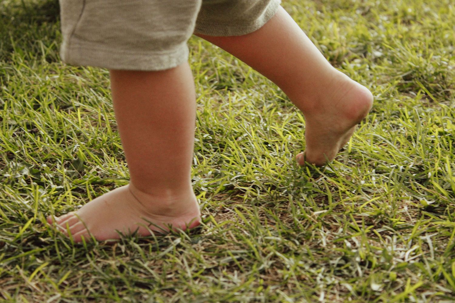 Small bare feet walking on green grass captured in a sequence of photos.