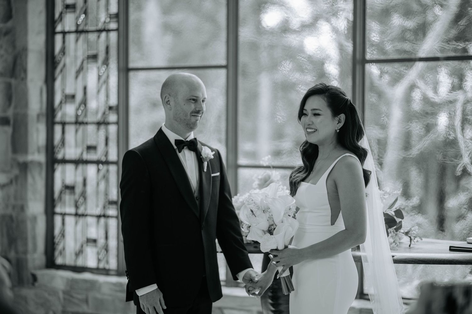 A black and white wedding photo showing a couple sharing a joyful moment together in an elegant indoor setting.