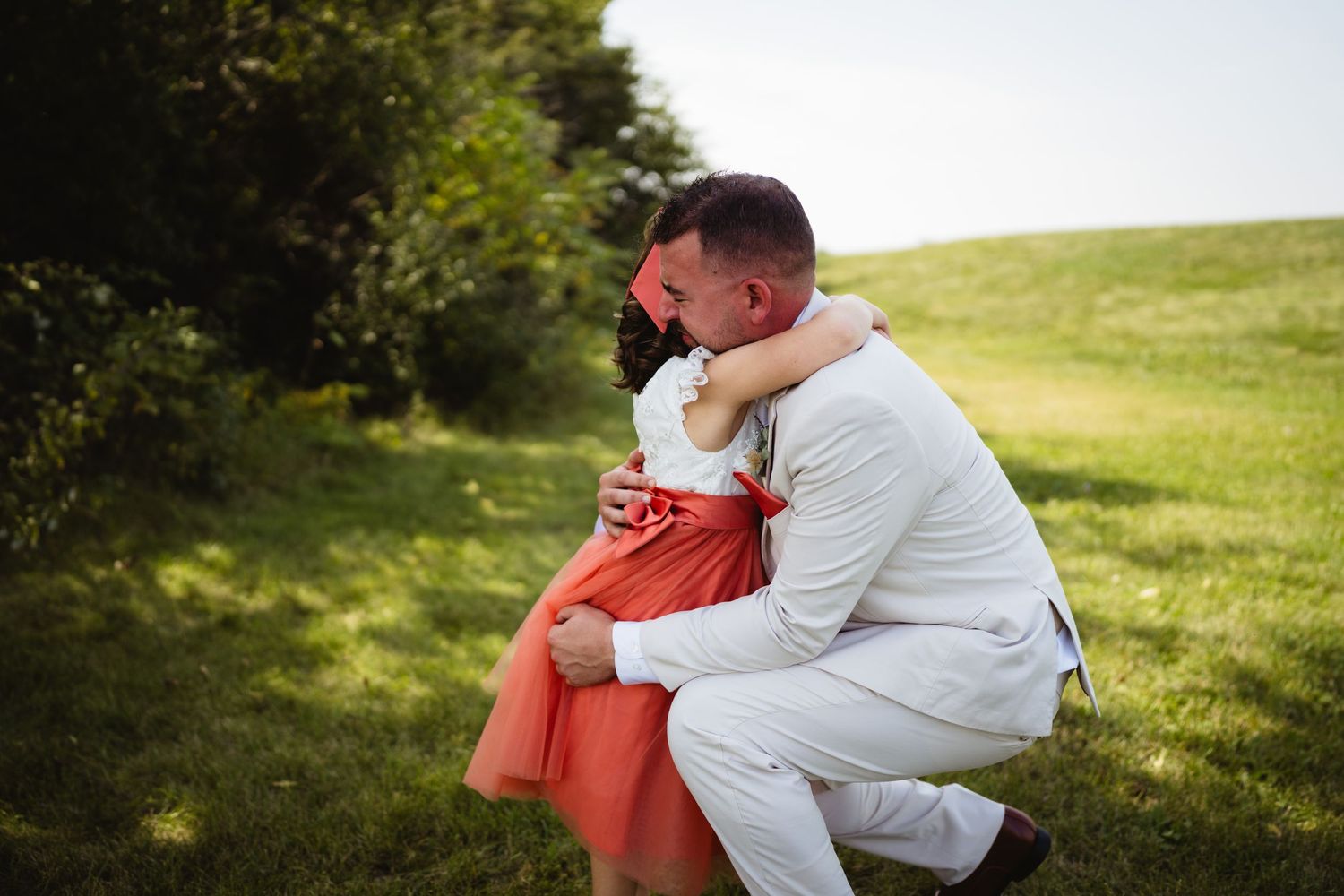 A couple sits together in a grassy field during a bright summer day, showing tender affection and closeness.