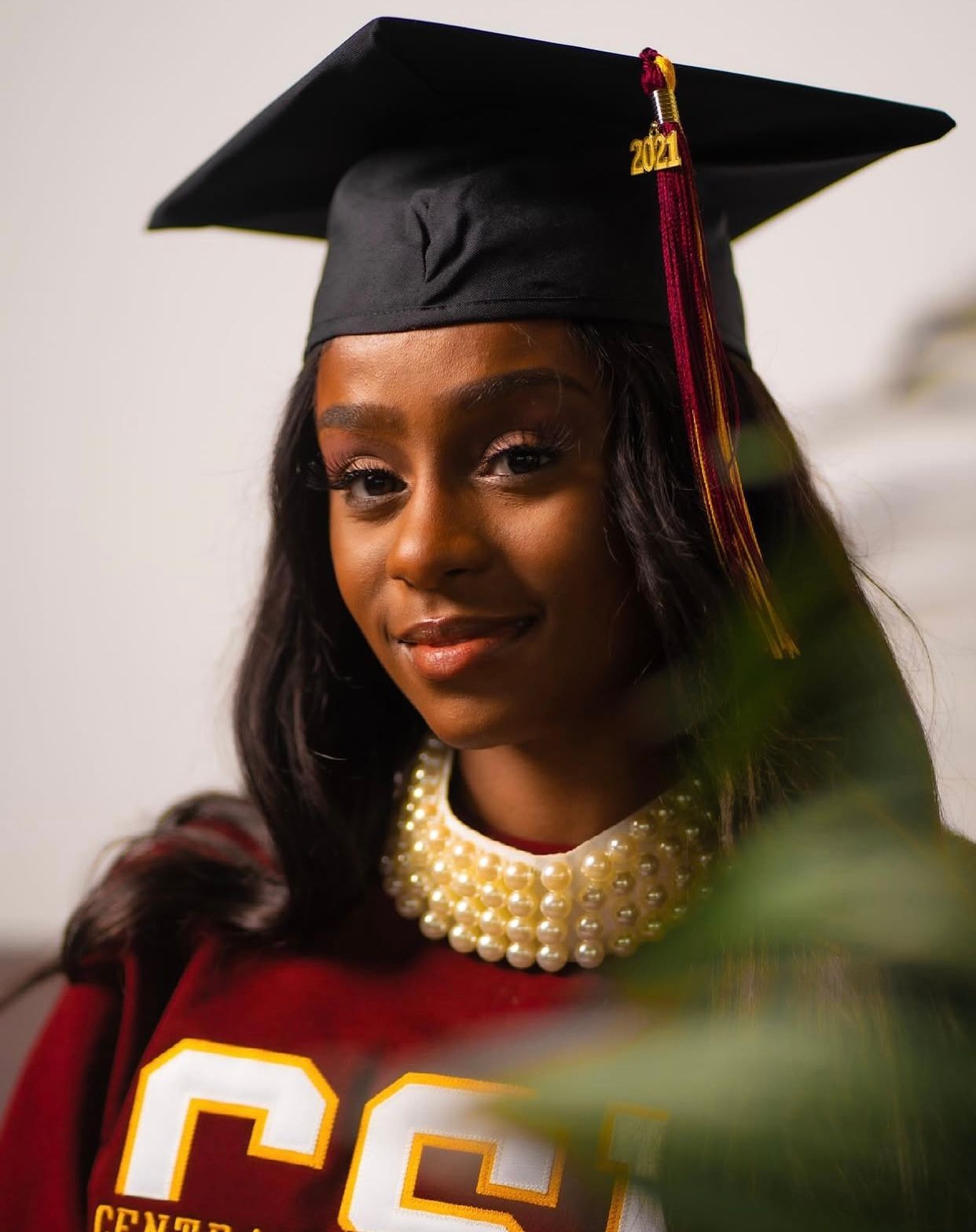 Graduate wearing a black cap and gown with a pearl necklace and maroon tassel during commencement ceremony.