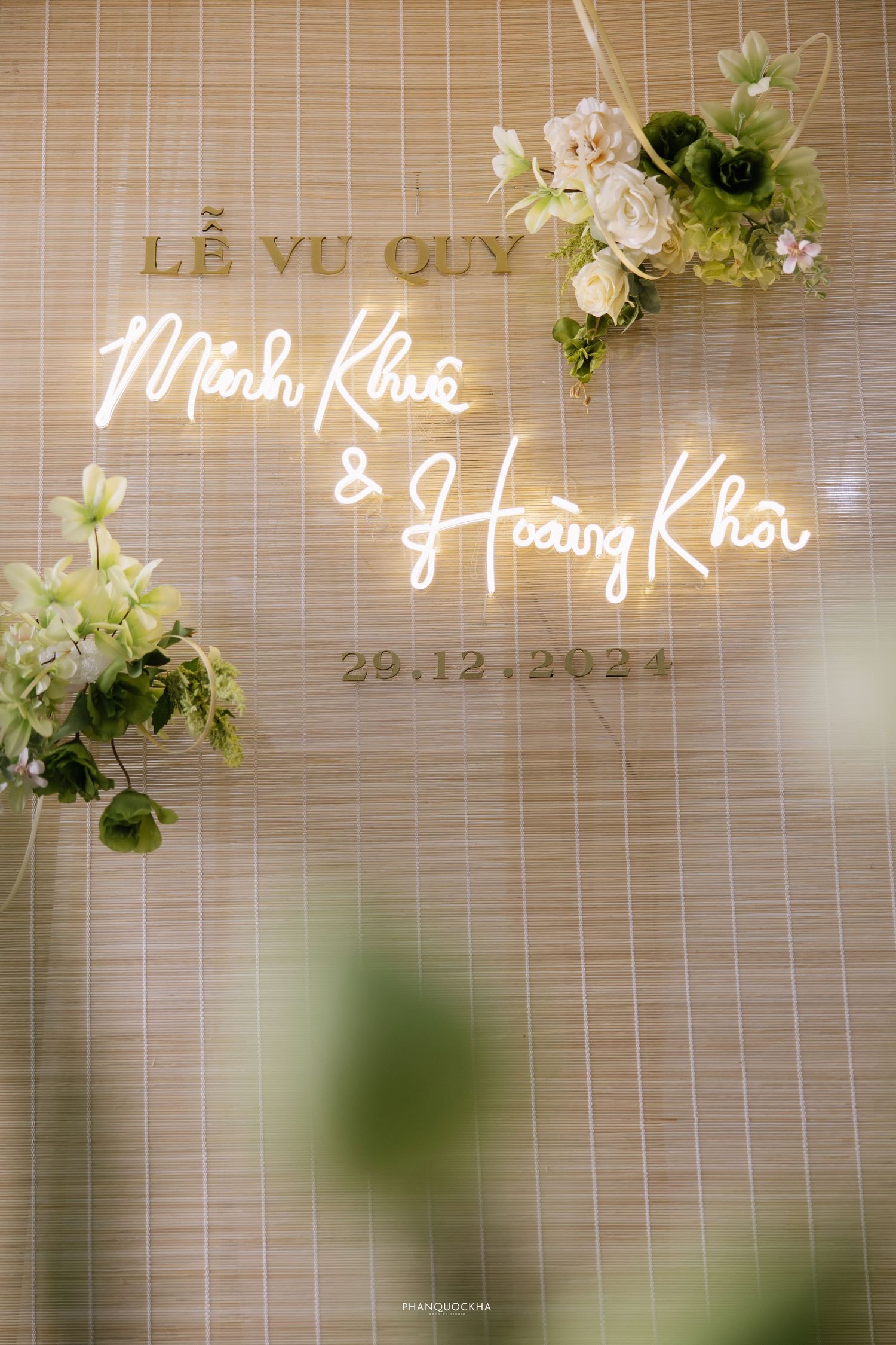 Elegant wedding sign reading Le Vu Quy Minh Khue and Hoang Khoi dated 29.12.2024 with green floral decor.