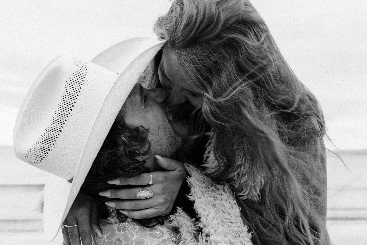 A romantic proposal unfolds along a scenic coastal cliff with mountains and ocean views at golden hour.