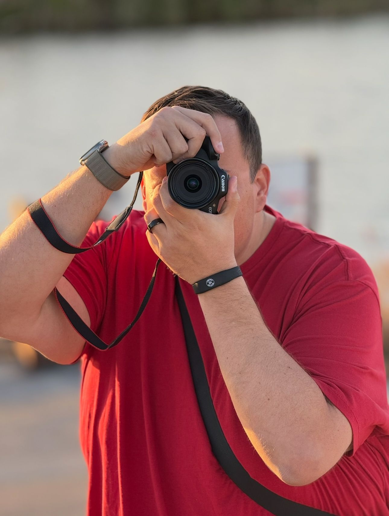 Person in red shirt taking photos with a camera against blurred background.