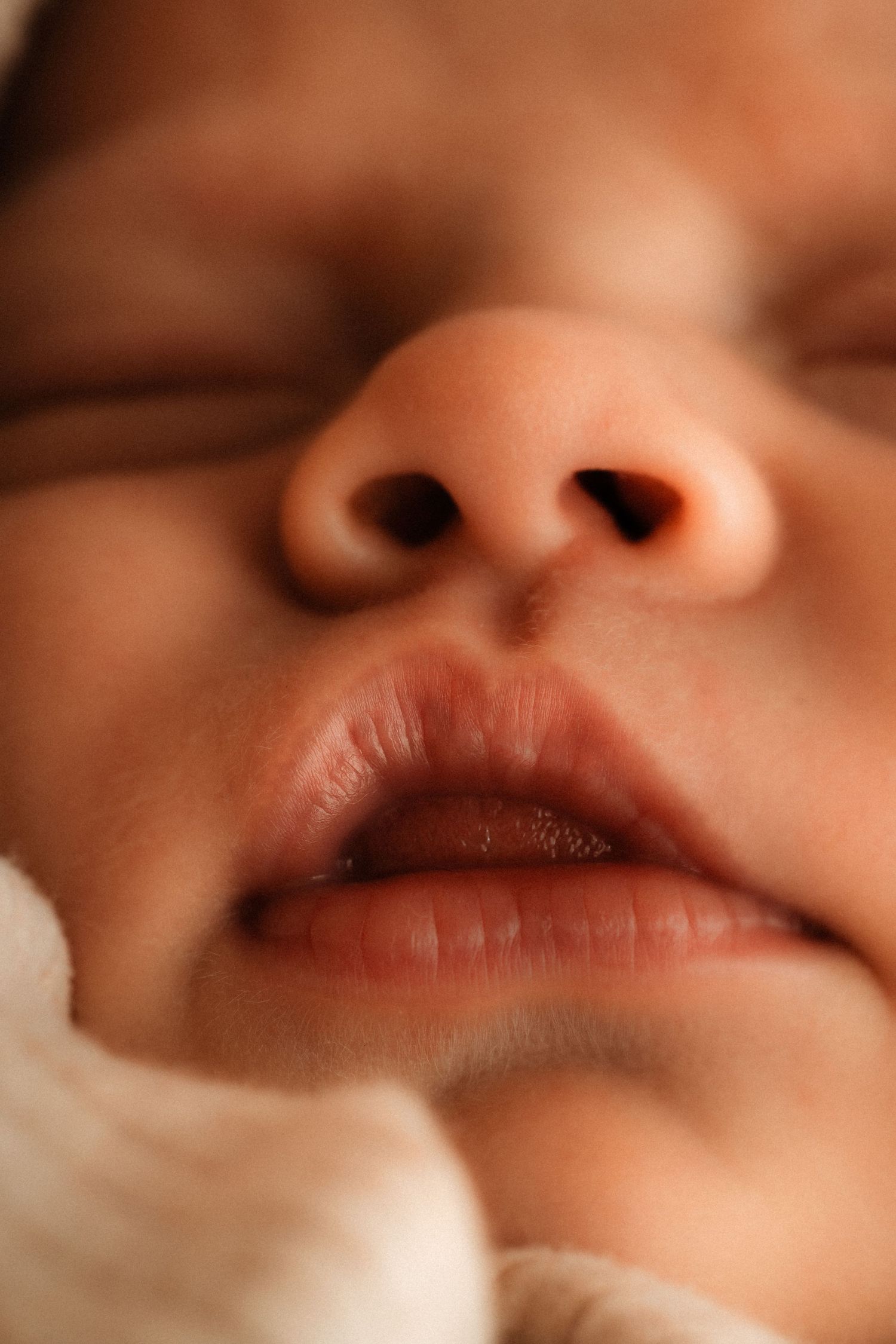 Newborn session, a Close-up macro photograph showing the nose and lips of an infant in soft lighting with Photographer Javea