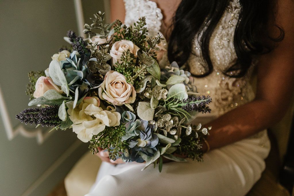 Elegant wedding floral arrangements featuring cream roses and greenery displayed in rustic wedding decor.