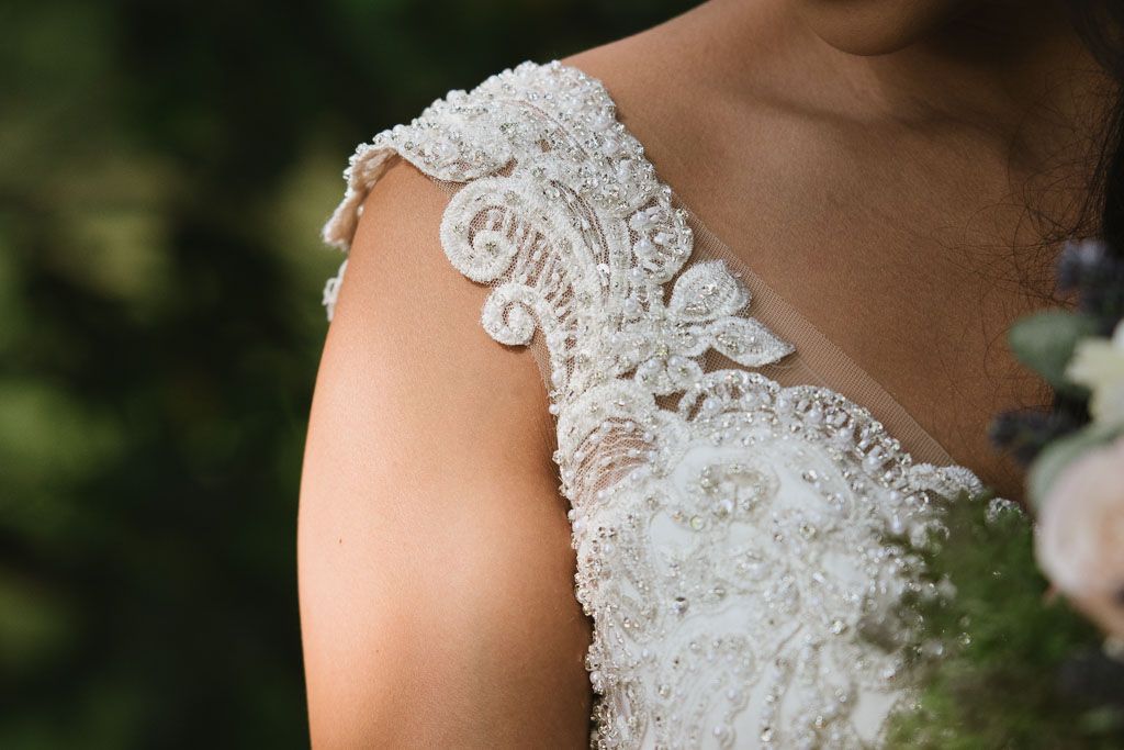 Close-up detail of delicate white lace and beading on a wedding dress shoulder strap.