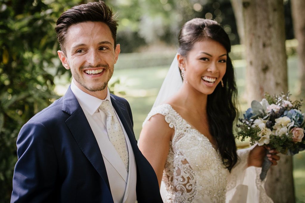 Joyful wedding couple shares candid moments during outdoor photo session surrounded by greenery.