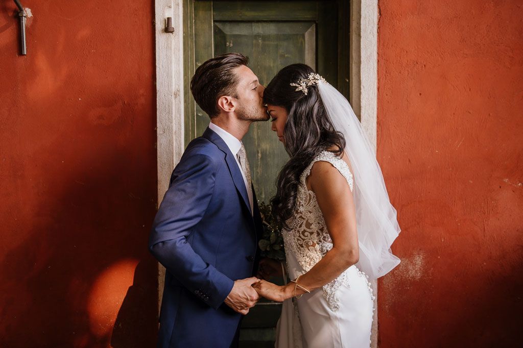 A romantic wedding moment against a vibrant red wall with traditional architecture details.