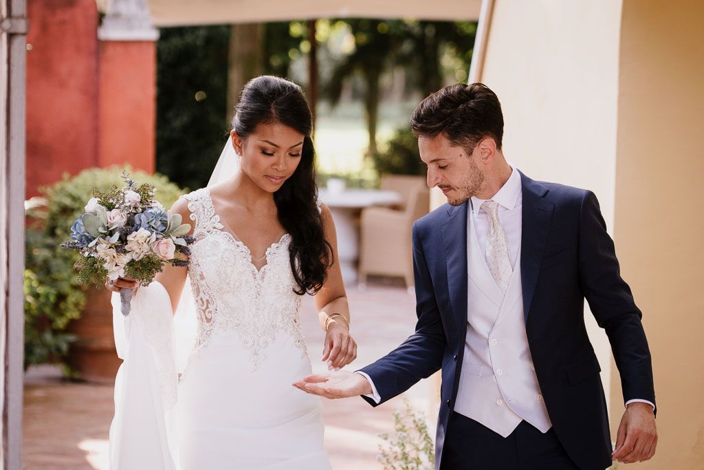 A bride and groom share a romantic wedding moment under an outdoor archway decorated with white florals.