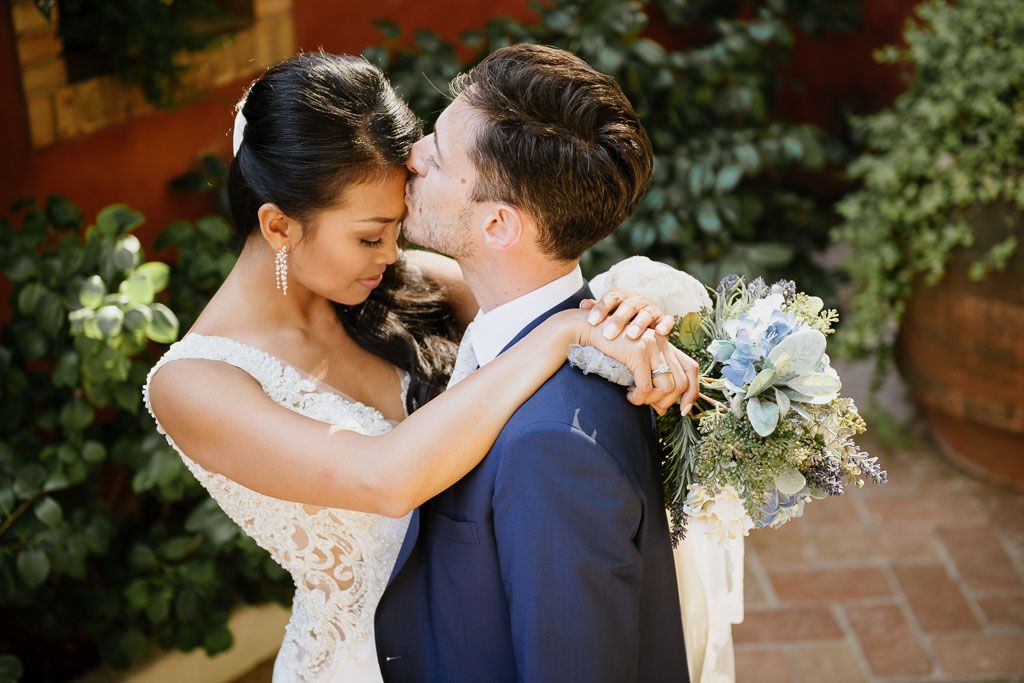 A couple in wedding attire embrace in an intimate moment during their outdoor garden ceremony.
