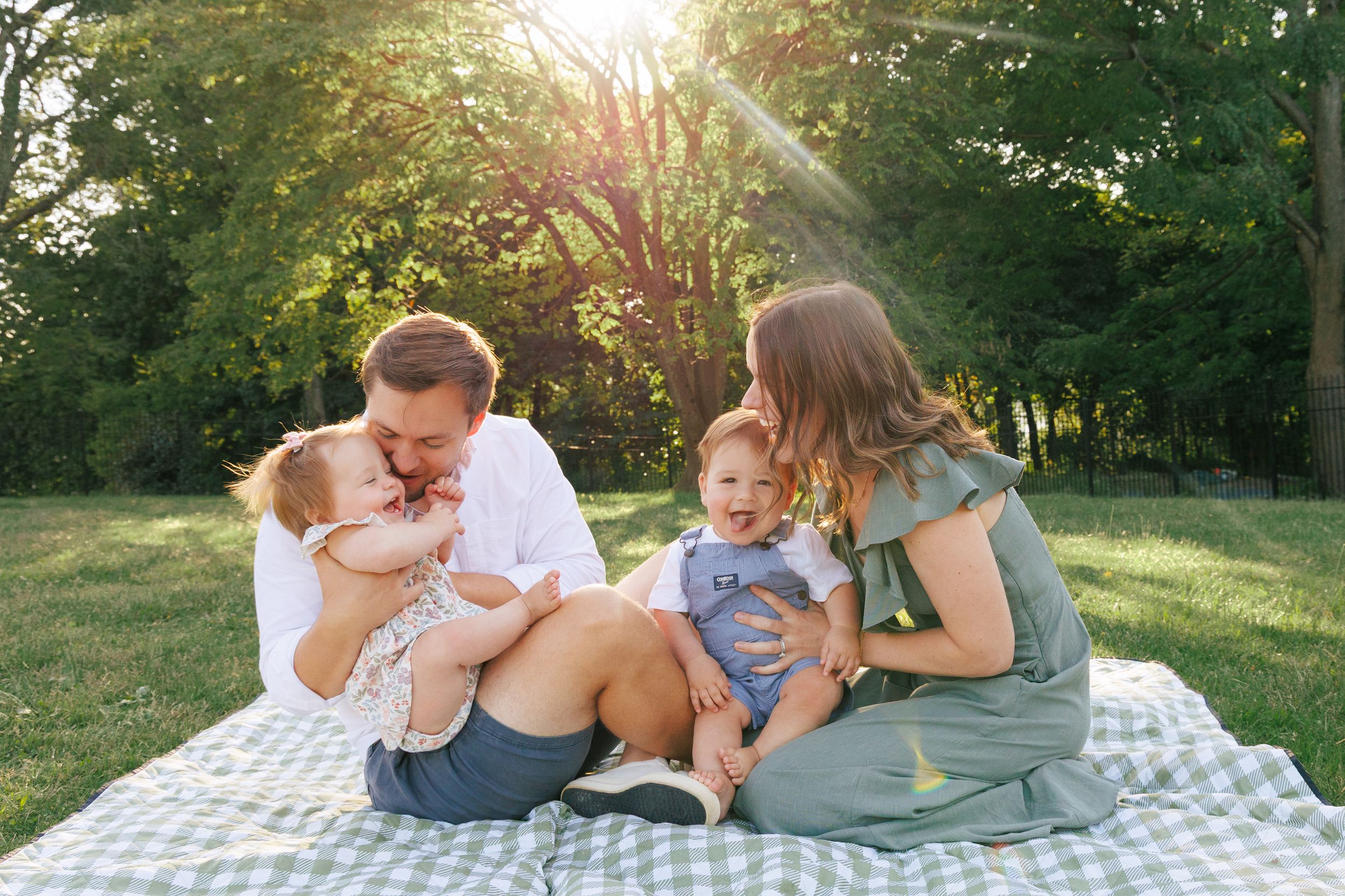 Family relaxing together on a picnic blanket during golden hour in a grassy field.